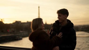 Romantik bir çift Paris 'teki Seine Nehri' nin üzerindeki bir köprüde Eiffel Kulesi 'nin arka planında gün batımında görülebildiği altın saat ışığı seyahat romantizmi ve bir aşk hikayesi için mükemmel sıcak ve davetkar bir atmosfer yaratır..