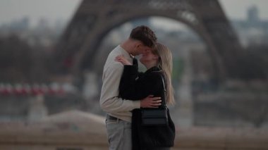 Paris 'te sevgi dolu bir çift arka planda Eyfel Kulesi ile Fransa' yı kucaklıyor. Genç çift ikonik simgelerin önünde birbirlerine sarılıyor ve sevgi gösteriyorlar..