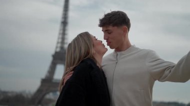 Paris 'te Eyfel Kulesi' nin önünde romantik bir çift öpüşür genç aşıklar sevgi ve beraberliği kucaklarlar ikonik bir dönüm noktası karşısında Aşk sevinci ve kutlama anını yakalar