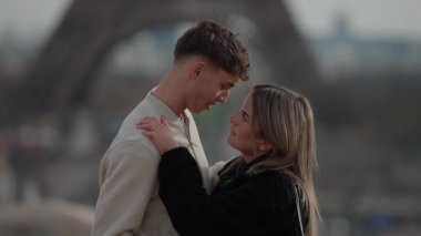 Paris 'te genç bir çift, arka planda Eiffel Kulesi' nin bulanıklığıyla Fransa 'yı kucaklıyor. Aşıklar, yumuşak doğal aydınlatmayla samimi bir anı paylaşıyorlar..