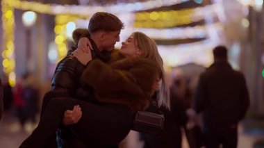 Geceleri Paris 'te romantik bir çift, kadını kollarında taşır Bokeh ışıkları şehrin sokaklarını aydınlatırken sevgi dolu ve romantik bir atmosfer yaratır..