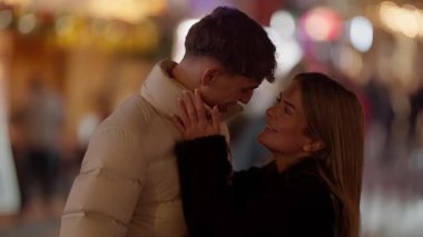 Genç bir çift gece Paris 'te romantik bir öpücüğü paylaşıyor. Arka plandaki bulanık ışıklar yumuşak bir bokeh etkisi yaratıyor. İki aşık arasındaki samimi ve sevgi dolu anı güçlendiriyor..