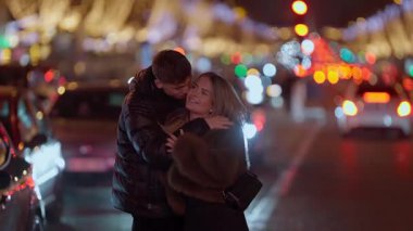 Romantik bir çift Paris 'te bir caddede sarılır gece vakti Bokeh ışıkları arka planda arabaların geçişi gibi sahneyi aydınlatır çift ışıklar şehrinde sevgi ve şefkat anlarını paylaşır.