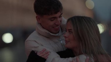 Paris 'te genç bir çift alacakaranlıkta Fransa' da sarılıyor. Erkek ve kadın arka planda yumuşak bokeh ışıklarıyla sarılıyorlar. Romantizm ve sevgi dolu samimi bir anı paylaşıyorlar..