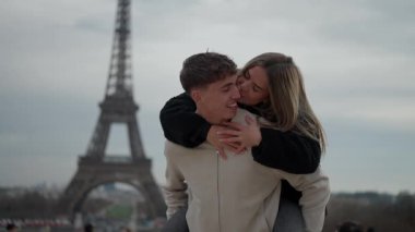 Romantik bir çift, arka planda Eyfel Kulesi ile Paris 'te gezintiden zevk alır. Genç kadın, sevgilerini ve sevgilerini gösteren erkeği kucaklar. Bu klip bir seyahat tatili ve yavaş çekim konseptini yakalar.