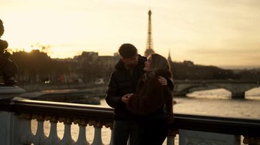 Romantik bir çift, Paris 'te arka planda Eyfel Kulesi' ne sarılır. Gün batımında Fransa 'da altın saat ışığı, sıcak ve sevgi dolu bir atmosfer yaratır..