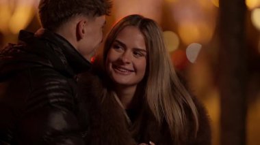 Genç bir çift gece Paris 'te sarılıyor kadın gülümsüyor ve kürk manto giyiyor erkek ceket giyerken Bokeh ışıkları romantik bir atmosfer yaratıyor klipler çift arasında bir aşk anı ve bağ kuruyor..