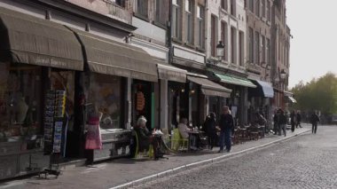 BRUGES, BELGIUM - 15 Eylül 2025 - İnsanlar Bruges 'deki bir kaldırım taşı caddesi boyunca bulunan kafelerde ve dükkanlarda oturmayı seviyor