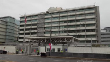 SEOUL, Güney Kore - 11 Ekim 2025 - ABD Büyükelçiliği binası, ABD bayrağı dalgalanan, bulutlu bir günde güvenlik personeli