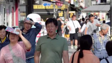 BUSAN, Güney Kore - 10 EKİM 2025 Busan 'da kalabalık bir sokakta yürüyen insanlar, parlak yaz güneşinden korunuyorlar.