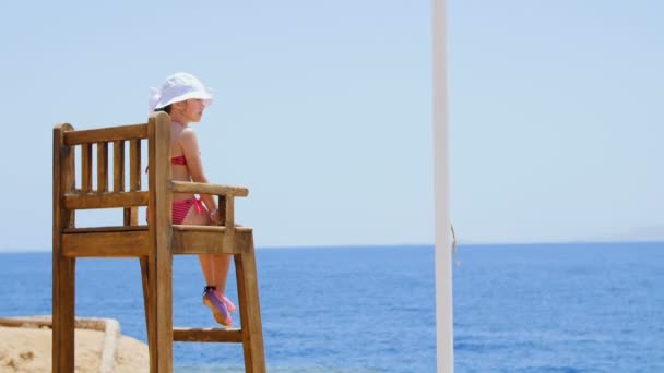 Hermosa niña en una silla mirando al mar — Vídeo de stock