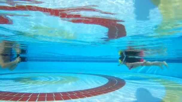 Een klein meisje en een fotograaf in het zwembad onderwater — Stockvideo