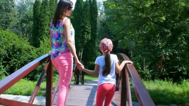 Mother and daughter go on the bridge in the park — Stock Video