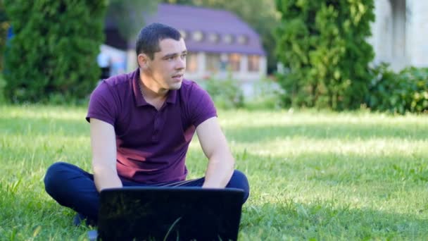 Młody mężczyzna pracujący z laptopa na trawniku — Wideo stockowe