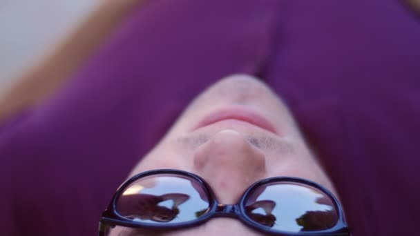 Beautiful girl dancing for the young guy - reclining on a bench in the park, reflected in glasses — Stock Video