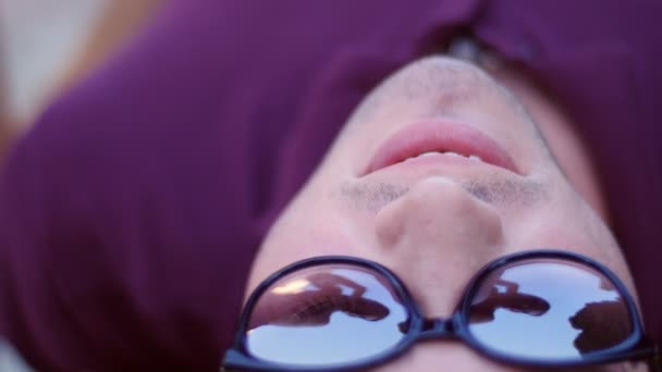 Hermosa chica endereza su cabello - un reflejo de un joven con gafas acostado en un banco en el parque — Vídeo de stock