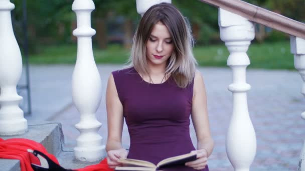 Όμορφο κορίτσι διαβάζοντας ένα βιβλίο που κάθομαι στις σκάλες — Αρχείο Βίντεο