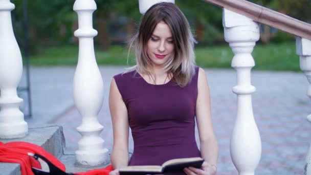 Schönes Mädchen liest ein Buch, das auf der Treppe sitzt — Stockvideo