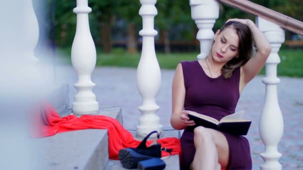 Hermosa chica leyendo un libro sentado en las escaleras — Vídeo de stock