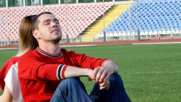 Un giovane uomo e una bella ragazza allo stadio sono seduti in mezzo al campo — Video Stock