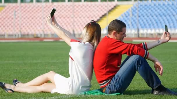 Ung kille och vacker flicka gör selfie sitter på fotbollsplan — Stockvideo