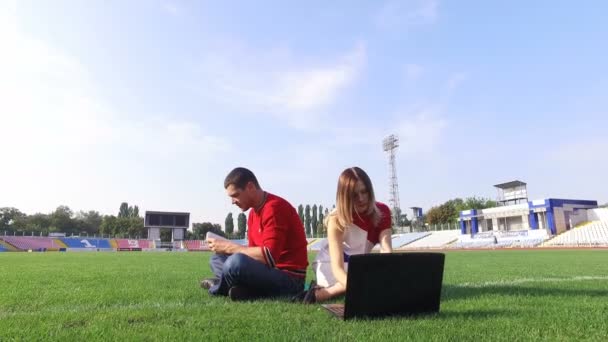 Hermosa chica trabajando en el ordenador portátil, hombre lee un libro en el estadio — Vídeos de Stock