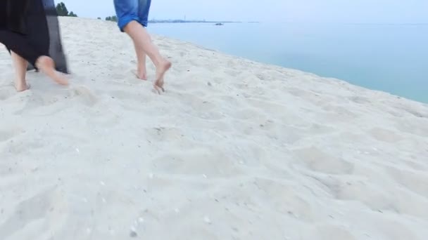 Menina bonita e seu namorado andando ao longo da costa os pés estão na areia — Vídeo de Stock