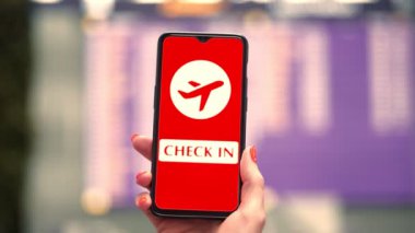 Uçak simgesi, giriş işareti olan akıllı telefonu havaalanının kalkış terminalinde, uçuş bilgi panosunun önünde, ekranda tutarken..