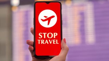 Uçak simgesiyle el ele tutuşan akıllı telefon, ekranda, kalkış terminalinde, havaalanındaki uçuş bilgi panosunun önünde,.