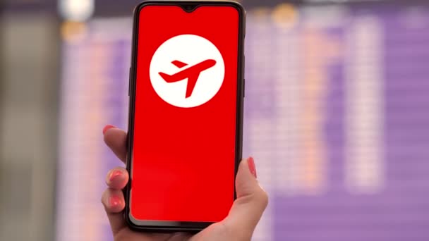 Gros plan du smartphone portable avec icône de l'avion, aucun signe de vacances, à l'écran, devant le tableau d'information de vol dans le terminal des départs, à l'aéroport. — Video