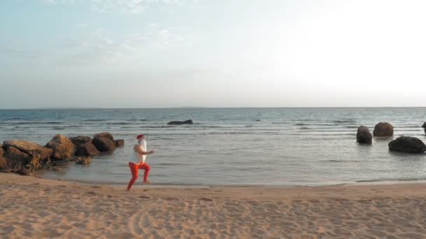 有趣的圣塔爪。海边的桑塔 · 克洛斯。桑塔 · 克劳斯匆匆离去。穿着T恤衫和红腿的桑塔 · 克洛斯跑来跑去，沿着海滨疾驰去。炎热的夏天. — 图库视频影像