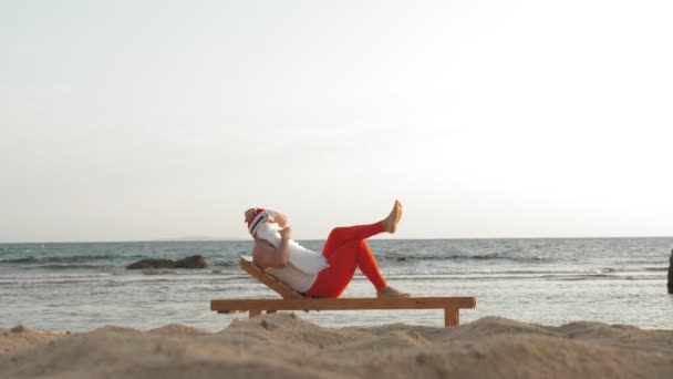 Vicces télapó napozik. Santa fekszik fa nyugágyon a tengerparton, és iszik egy finom koktélt. Santa Claus nyári vakáción van a tengerparton.. — Stock videók