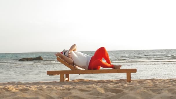 Santa Claus divertido toma el sol. santa, en gafas de sol, se encuentra en una tumbona de madera en la playa junto al mar. Duerme y se relaja. Santa Claus está de vacaciones de verano, en la orilla del mar — Vídeos de Stock