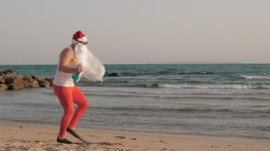 Noel Baba yaz tatili. Noel Baba eğleniyor. Güneş gözlüklü ve paletli komik Noel Baba, sahilde dans ediyor ve dinleniyor. Noel Baba şnorkelle dalacak