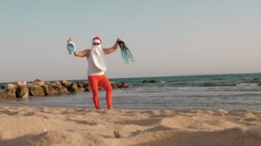 Noel Baba yaz tatili. Noel Baba eğleniyor. Komik Noel Baba, güneş gözlüklü, yüzgeçli ve şnorkelli, deniz kenarında dans ediyor. Noel Baba şnorkelle dalacak