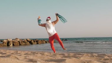 Noel Baba yaz tatili. Noel Baba eğleniyor. Komik Noel Baba, güneş gözlüklü, yüzgeçli ve şnorkelli, deniz kenarında dans ediyor. Noel Baba şnorkelle dalacak