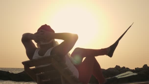 Jultomten sommarsemester. Jultomten solar. Bakåt. Rolig Santa, i flippers, sitter på solstol, på stranden vid havet och njuta av solnedgången eller soluppgången, avkopplande. vid stranden.. — Stockvideo