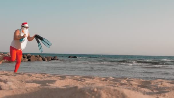 Jultomten sommarsemester. Jultomten har roligt. Rolig Santa, i solglasögon, med flippers och snorkling mask, löper längs stranden. Han har bråttom att simma, snorkel.. — Stockvideo