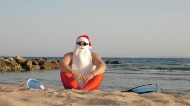 Noel Baba yaz tatili. Noel Baba eğleniyor. Noel Baba yoga yapıyor. Komik Noel Baba, güneş gözlüklü, yüzgeçli ve şnorkelli, deniz kenarında. Noel Baba şnorkelle dalacak