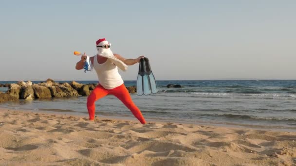 Der Weihnachtsmann im Sommerurlaub. Der Weihnachtsmann hat Spaß. Der Weihnachtsmann beim Yoga. Lustiger Weihnachtsmann mit Sonnenbrille, Schwimmflossen und Schnorchelmaske am Strand am Meer. Weihnachtsmann geht zum Schnorcheln — Stockvideo