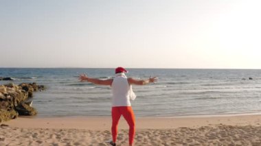 Noel Baba yaz tatili. Noel Baba eğleniyor. Komik Noel Baba, paletlerle kumlu sahilden denize koşuyor. Yüzmek için acele ediyor, şnorkel. arka plan