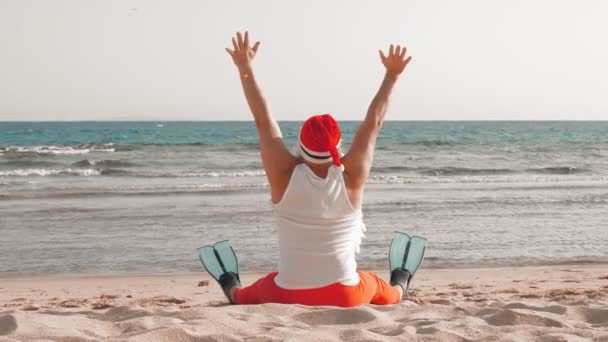 Papai Noel férias de verão. Papai Noel se divertindo. Engraçado Papai Noel, de barbatanas, relaxante enquanto sentado na praia de areia junto ao mar. vista para trás. — Vídeo de Stock