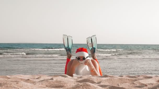 Wakacje Świętego Mikołaja. Święty Mikołaj dobrze się bawi. Śmieszny Mikołaj, w płetwach, relaksujący leżąc na piaszczystej plaży nad morzem. — Wideo stockowe