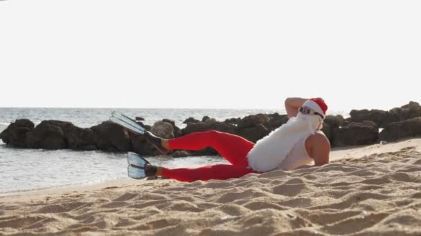 Santa Claus summer vacation. Santa Claus having fun. Funny Santa, in flippers, relaxing while lying on sandy beach by the sea. — Stock Video