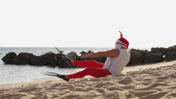 Liburan musim panas Santa Claus. Santa Claus bersenang-senang. Funny Santa, dalam sirip, santai saat berbaring di pantai berpasir oleh laut. — Stok Video