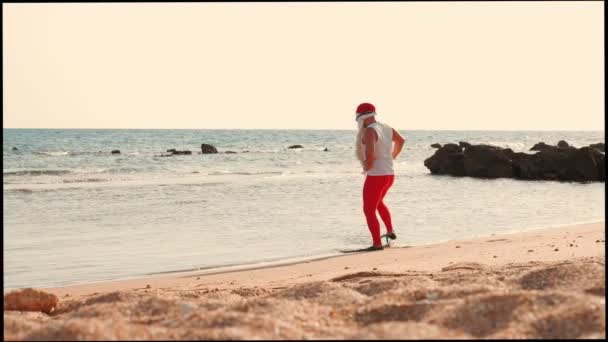 Kerstman zomervakantie. De kerstman heeft plezier. Grappige Kerstman, in zonnebrillen en flippers, komt langzaam in het zeewater van het zandstrand, staat op het punt om te zwemmen. — Stockvideo