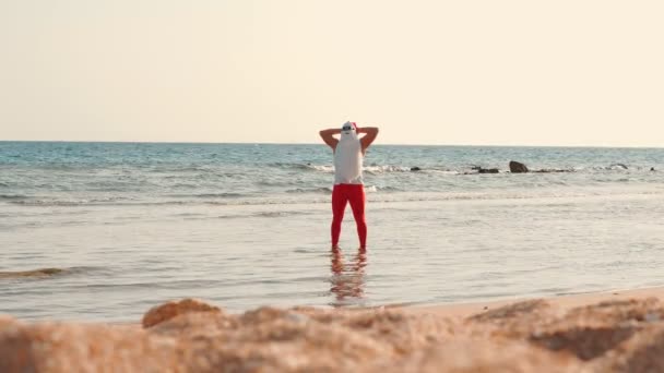 Kerstman zonnebaden. De kerstman heeft plezier. Grappige Kerstman, in een zonnebril, staand in zeewater op het strand. Kerstman zomer vakantie — Stockvideo