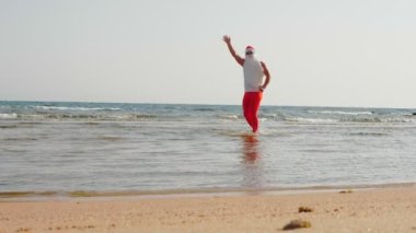 Komik Noel Baba. Noel Baba, güneş gözlüğü ve yüzgeçleriyle el sallayarak kumsalın yanındaki deniz suyunda eğleniyor. Noel Baba yaz tatili.