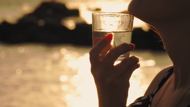 Szklanka wody o zachodzie słońca. zbliżenie. sylwetka. Kobieta trzyma szklankę czystej wody na szyi. tło zachodu słońca lub wschodu słońca nad morzem — Wideo stockowe