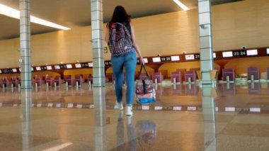 Gezgin gecikmiş uçuş için bekliyor. Kadın bavuluyla terk edilmiş salondan boş havaalanındaki kapalı gişelere doğru yürüyor. Coronavirüs salgını nedeniyle uçuş iptal edildi.